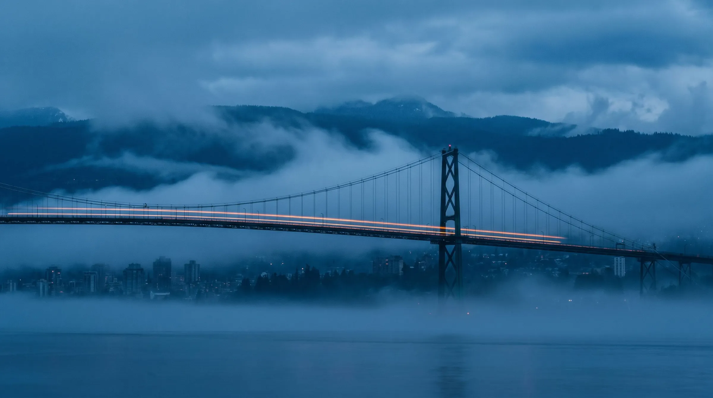 Lions Gate Bridge in Vancouver at blue hour with a single orange light trail